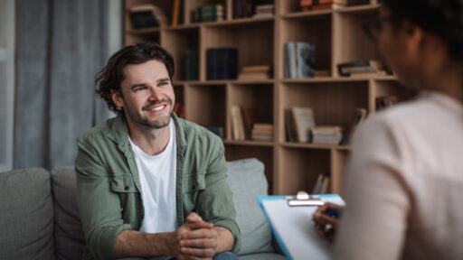 Millennial black woman psychologist consults smiling european guy in modern clinic interior. Solving of psychological problems, mental therapy and treatment, professional medical help and support