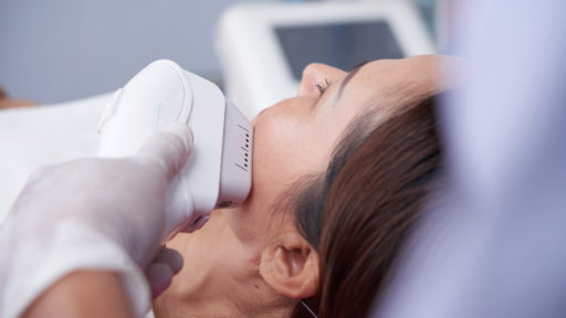 Image of a cosmetologist removing facial hair of female client with laser apparatus.