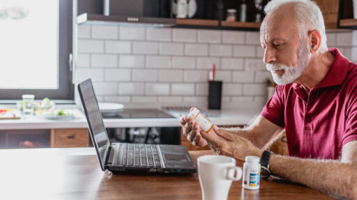 Senior man is looking for information about the medicine over the Internet. He is holding a medicine in one hand