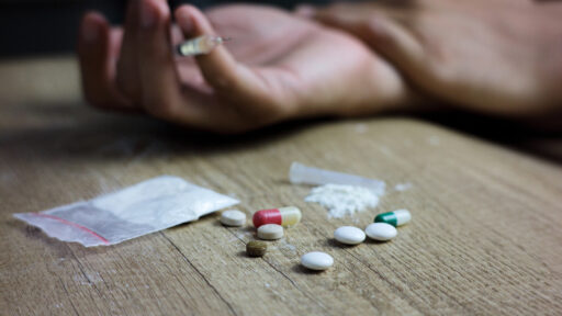 a hand that is holding a needle with pills scattered on the table