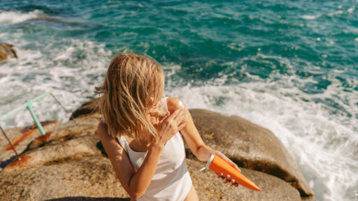woman putting on sunscreen while sitting by the water