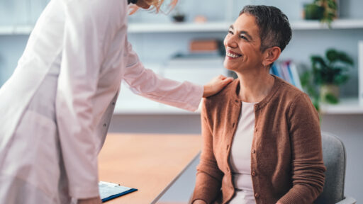 Patient sitting in a doctor's office smiling as the physician provides kind support. The interaction portrays a caring and professional medical environment fostering trust and compassion.