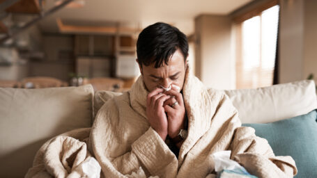 a man blowing his nose, snuggled in a blanket