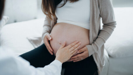 ropped shot of Asian pregnant woman having a consultation with doctor during routine check up at clinic. Doctor is performing an examination and touching the belly. Check-ups, tests and scans to ensure a healthy pregnancy for both mother and unborn baby