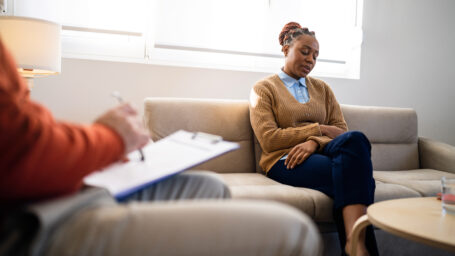 Young woman of Black ethnicity sitting on the couch, during psychotherapy, led by the male psychotherapist