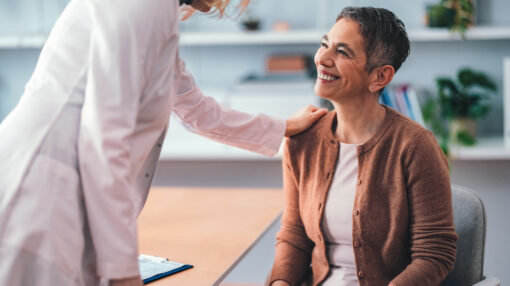 Patient sitting in a doctor's office smiling as the physician provides kind support. The interaction portrays a caring and professional medical environment fostering trust and compassion.