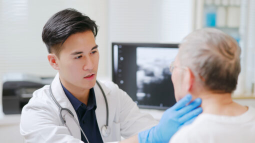 asian doctor is examining thyroid gland of elderly man through palpation by hands in hospital