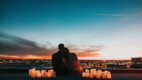Couple sitting close together watching a city sunset surrounded by candles