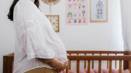 Pregnant woman cradling her belly beside a nursery crib