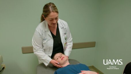 Physician at UAMS Northeast in Jonesboro examines a patient on an exam table while holding the patient's head.