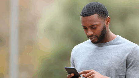 Man in a gray sweater looking down at his smartphone outdoors