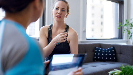 Candid image of a blond woman patient during a kinesiotherapy appointment with an asian female personal trainer to discuss training and physiotherapy to her shoulder