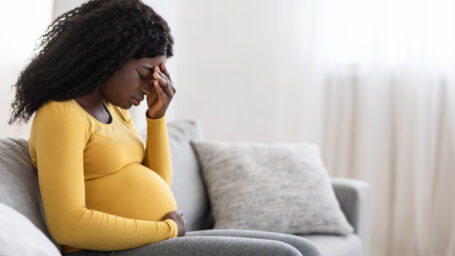Pregnant woman sitting on the couch with a migraine