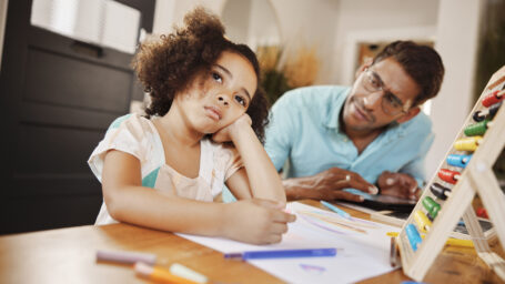 a little girl struggling to focus on her homework and a dad trying to help