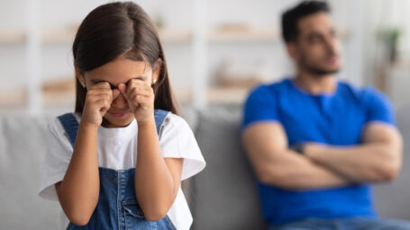 Little girl crying on the couch next to her father