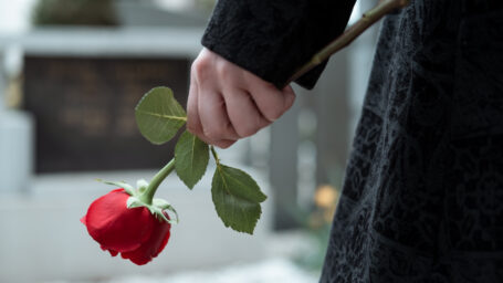 A woman carrying a rose while walking to a gravesite