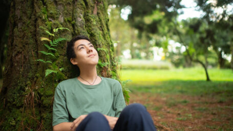 teen boy sitting at the base of a tree