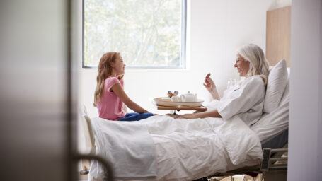 Granddaughter Visiting Grandmother In Hospital Bed For Afternoon Tea